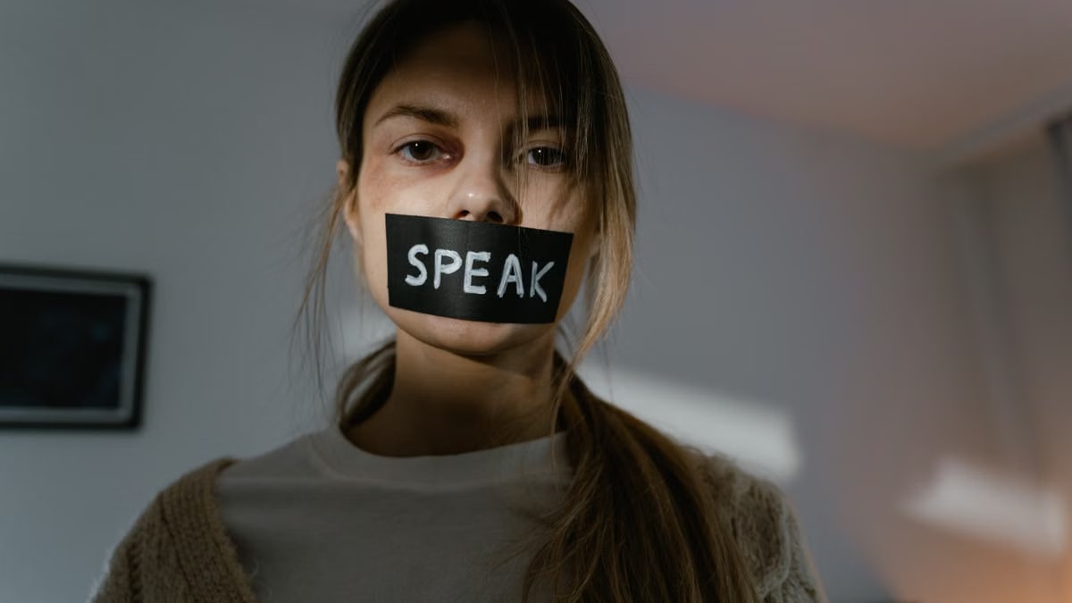 Woman with 'speak' tape over mouth.